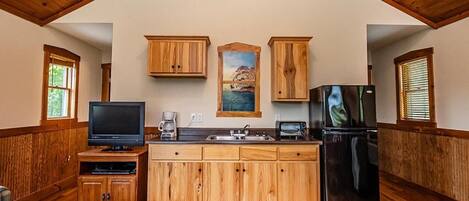 A kitchen with wooden cabinets, a refrigerator, a television, and a painting on the wall.