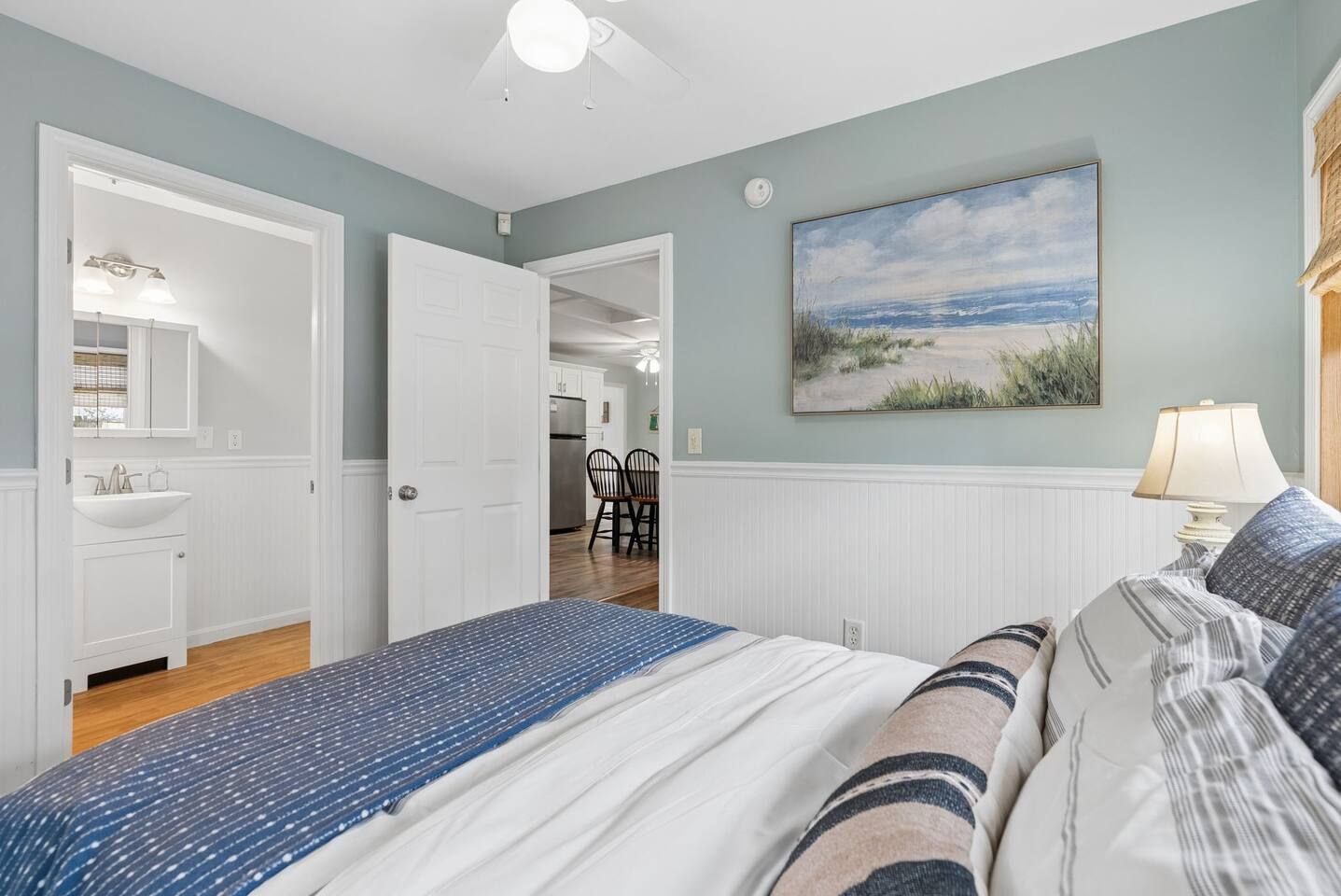 Une chambre avec un lit, un tableau représentant une plage et une vue sur la cuisine.