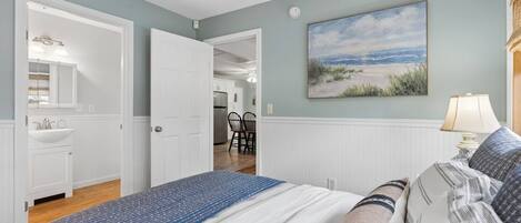 Une chambre avec un lit, un tableau représentant une plage et une vue sur la cuisine.