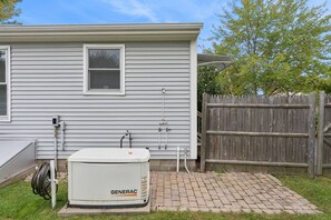 A residential property with a white exterior, a wooden fence, and a Generac water heater. - Pirate's Cove Cottage | beach, mini golf, backyard (Old Orchard Beach)