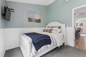 A bedroom with a white bed, a painting on the wall, and a door leading to a dining area. - Pirate's Cove Cottage | beach, mini golf, backyard (Old Orchard Beach)
