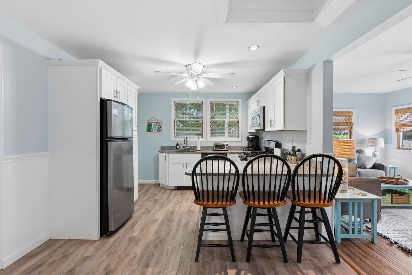 A modern kitchen with white cabinetry, a black refrigerator, and a ceiling fan.