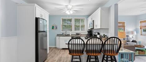 A modern kitchen with white cabinetry, a black refrigerator, and a ceiling fan.
