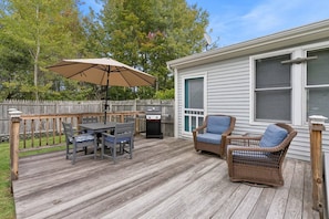 Une terrasse avec une table et des chaises, un barbecue et un fauteuil en osier.