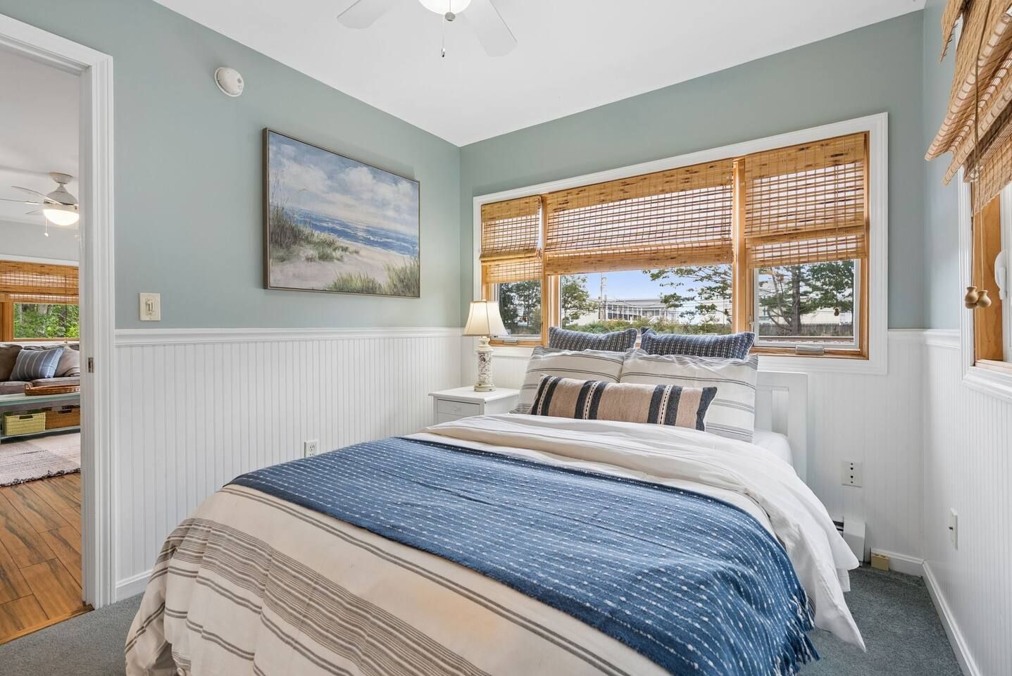 A bedroom with a bed, a window with blinds, a painting on the wall, and a ceiling fan.
