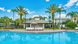 A swimming pool with lounge chairs and umbrellas, surrounded by palm trees and a building with a green roof. - The Epic 36208 Lake View Vista Cay Resort Orlando Florida (Orlando)