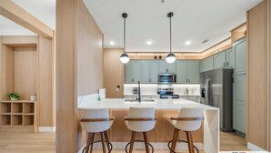 A modern kitchen with a central island, two bar stools, and wooden cabinetry. - The Epic 36208 Lake View Vista Cay Resort Orlando Florida (Orlando)