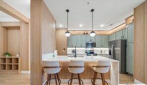 A modern kitchen with a central island, two bar stools, and wooden cabinetry. - The Epic 36208 Lake View Vista Cay Resort Orlando Florida (Orlando)