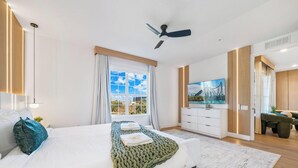 A modern bedroom with a bed, a ceiling fan, a TV, and a view of a park. - The Epic 48108 Lake View Vista Cay Resort Orlando Florida (Orlando)