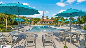 A poolside area with lounge chairs and umbrellas, a pool, and a building with a red roof in the background. - The Epic 48108 Lake View Vista Cay Resort Orlando Florida (Orlando)
