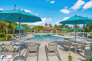 A poolside area with lounge chairs and umbrellas, a pool, and a building with a red roof in the background. - The Epic 48108 Lake View Vista Cay Resort Orlando Florida (Orlando)
