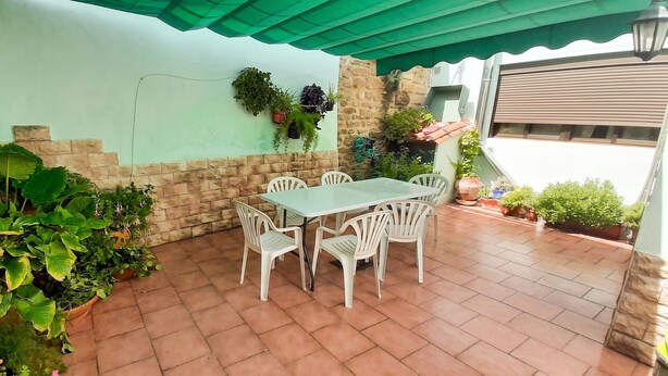 Eine Terrasse mit Tisch und Stühlen, umgeben von Kübelpflanzen und einer Steinmauer.