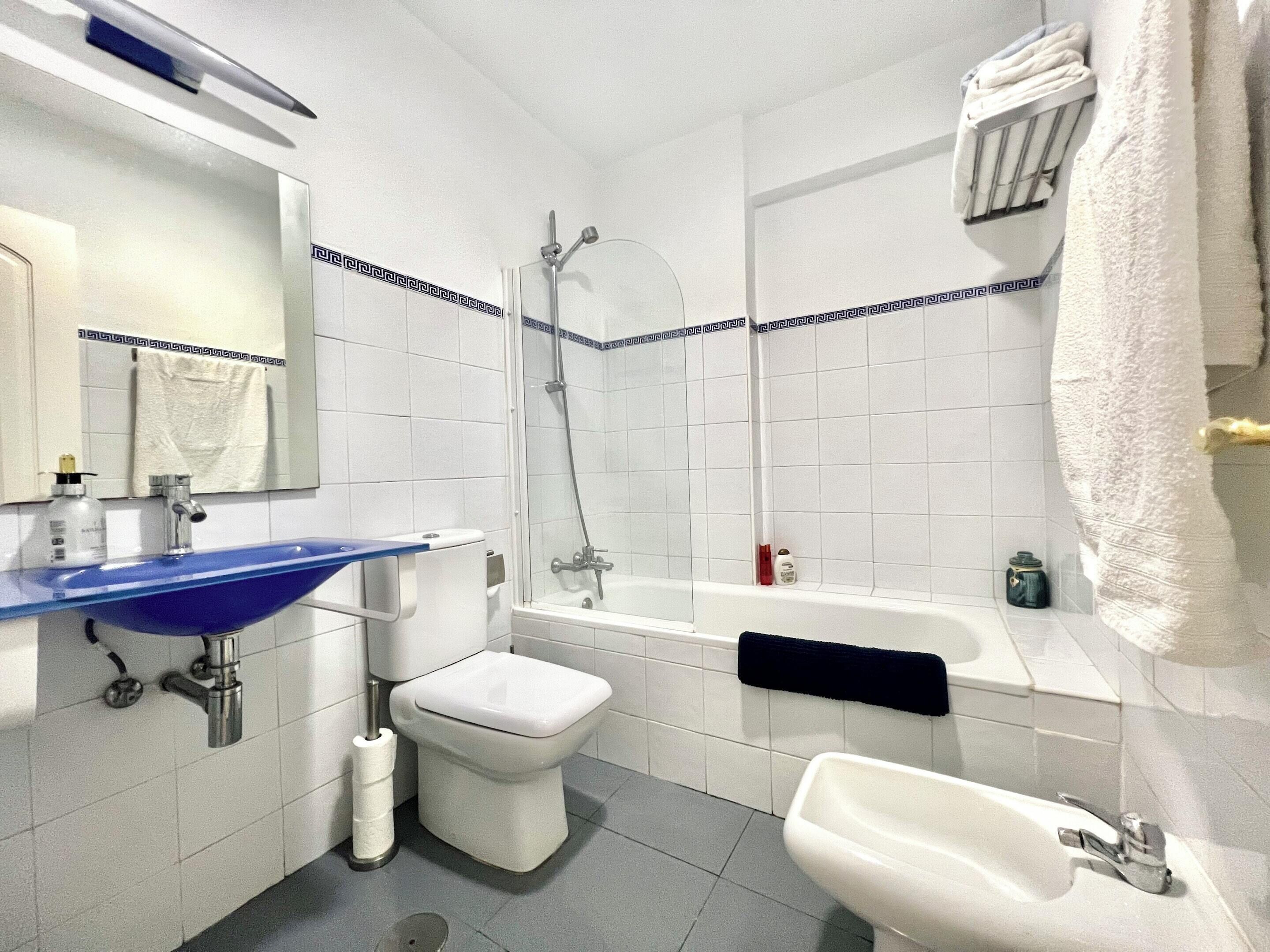 Une salle de bain avec un lavabo bleu, des toilettes blanches, une baignoire et un bidet.