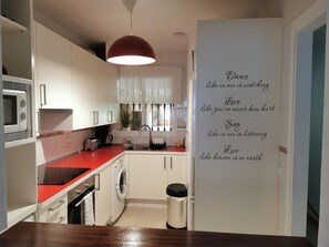 Une cuisine moderne avec des meubles blancs, un plan de travail rouge, un lave-linge et une poubelle.
