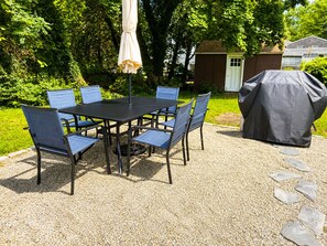 Une terrasse avec une table et des chaises, un barbecue et un espace abrité.