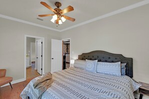 A bedroom with a large bed, a ceiling fan, and a door leading to a bathroom.