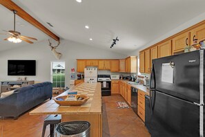 A modern kitchen with wooden cabinets, a black refrigerator, and a dining area with a blue sofa. - Two homes- 5 bedrooms on beautiful private lake. (Long Branch)