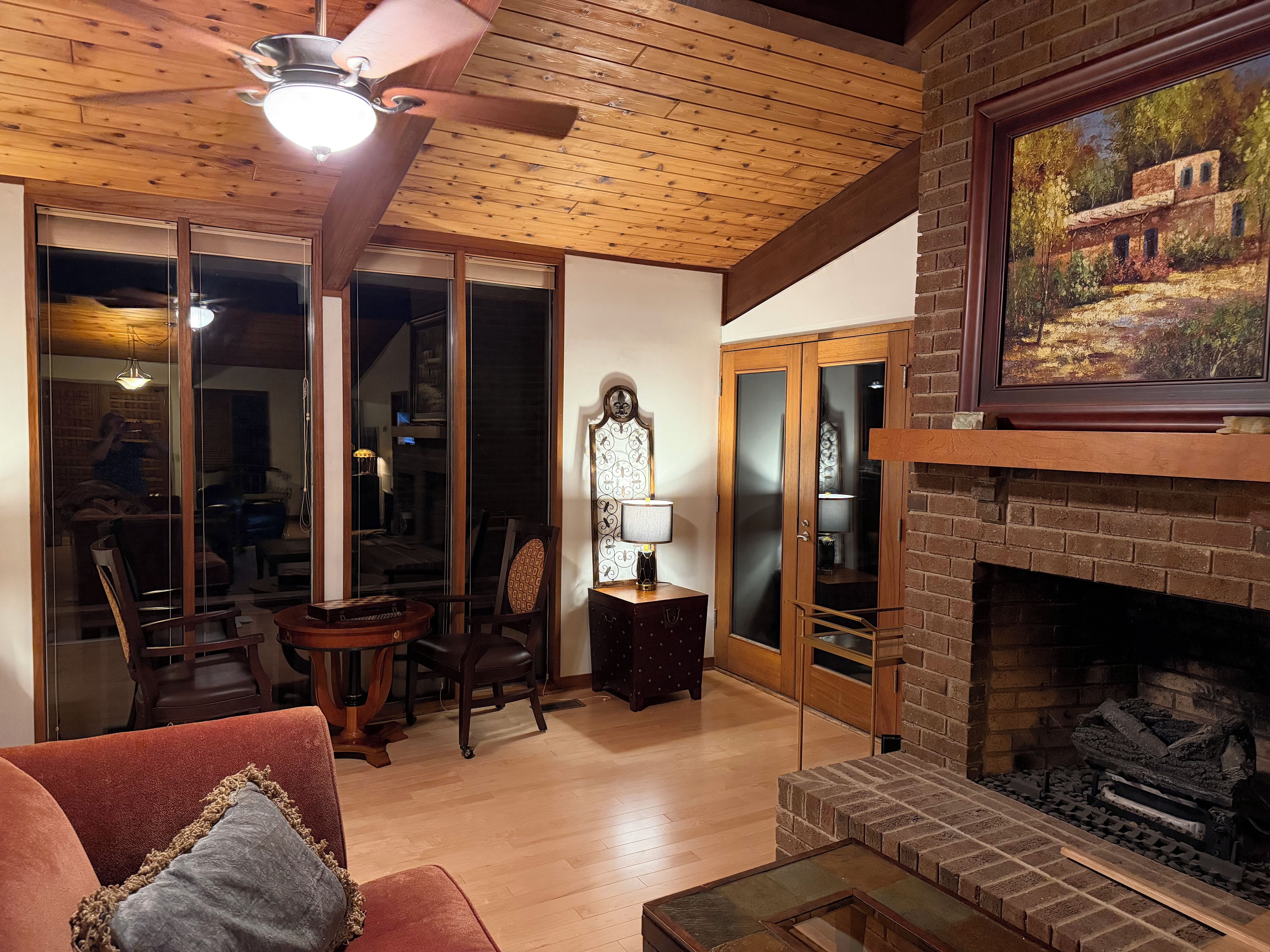 A cozy living room with a fireplace, wooden ceiling, and a dining area with a table and chairs.