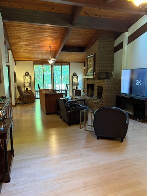 A spacious living room with a wooden floor, a fireplace, a television, and a dining area with a table and chairs. - Private gorgeous retreat on the golf course in Carolina Trace (Sanford)