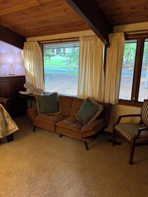 A cozy living room with a brown sofa, two green pillows, a wooden chair, and a lamp on a table. - Private gorgeous retreat on the golf course in Carolina Trace (Sanford)