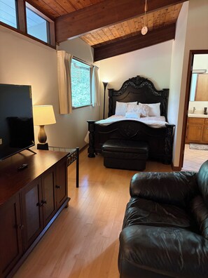 A bedroom with a wooden ceiling, a bed with a dark headboard, a television on a wooden cabinet, and a leather sofa. - Private gorgeous retreat on the golf course in Carolina Trace (Sanford)