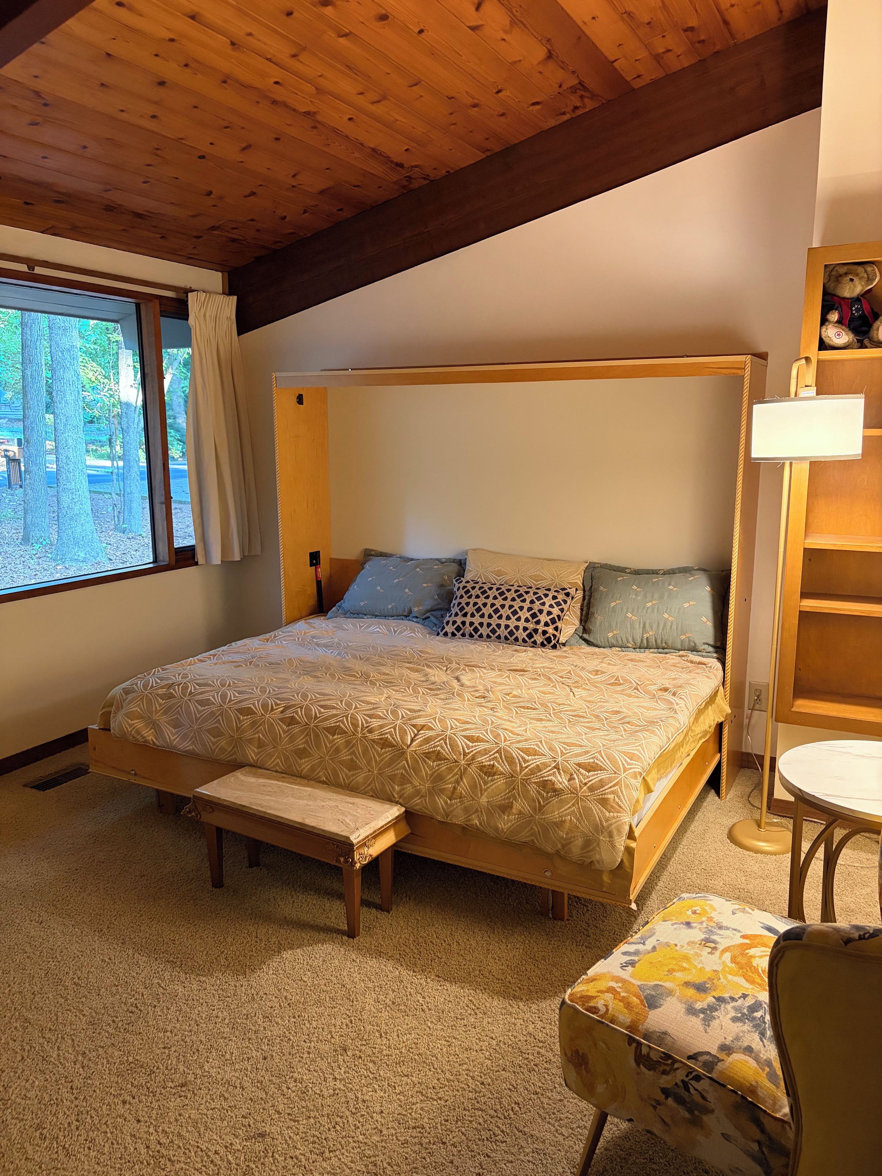 A bedroom with a wooden bed, a bench, a chair, and a window with curtains.