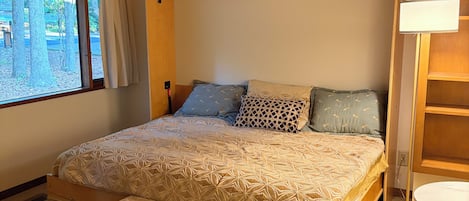 Un dormitorio con una cama de madera, un banco, una silla y una ventana con cortinas.