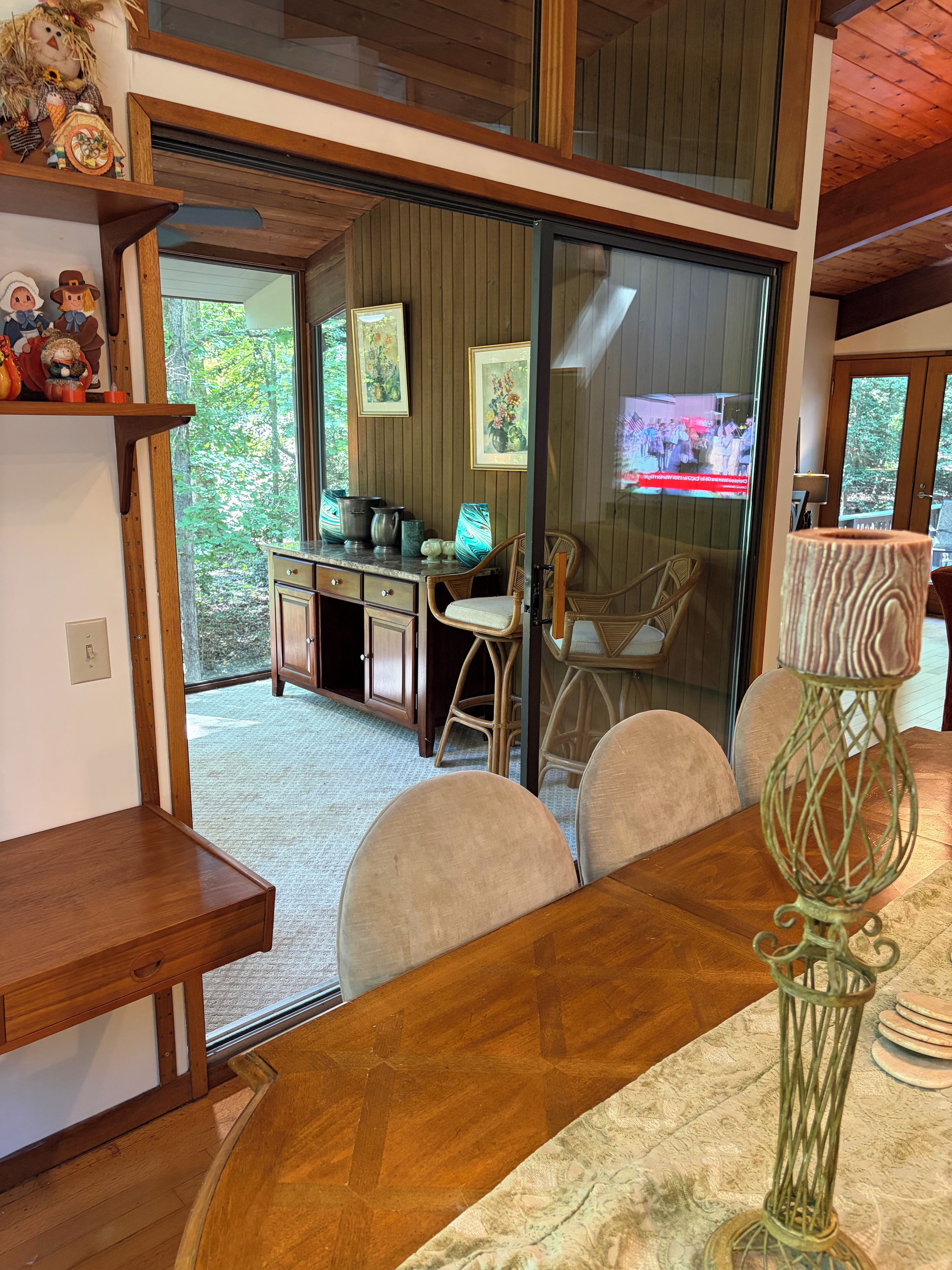 Un comedor con una mesa de madera, sillas, un florero y un televisor al fondo.