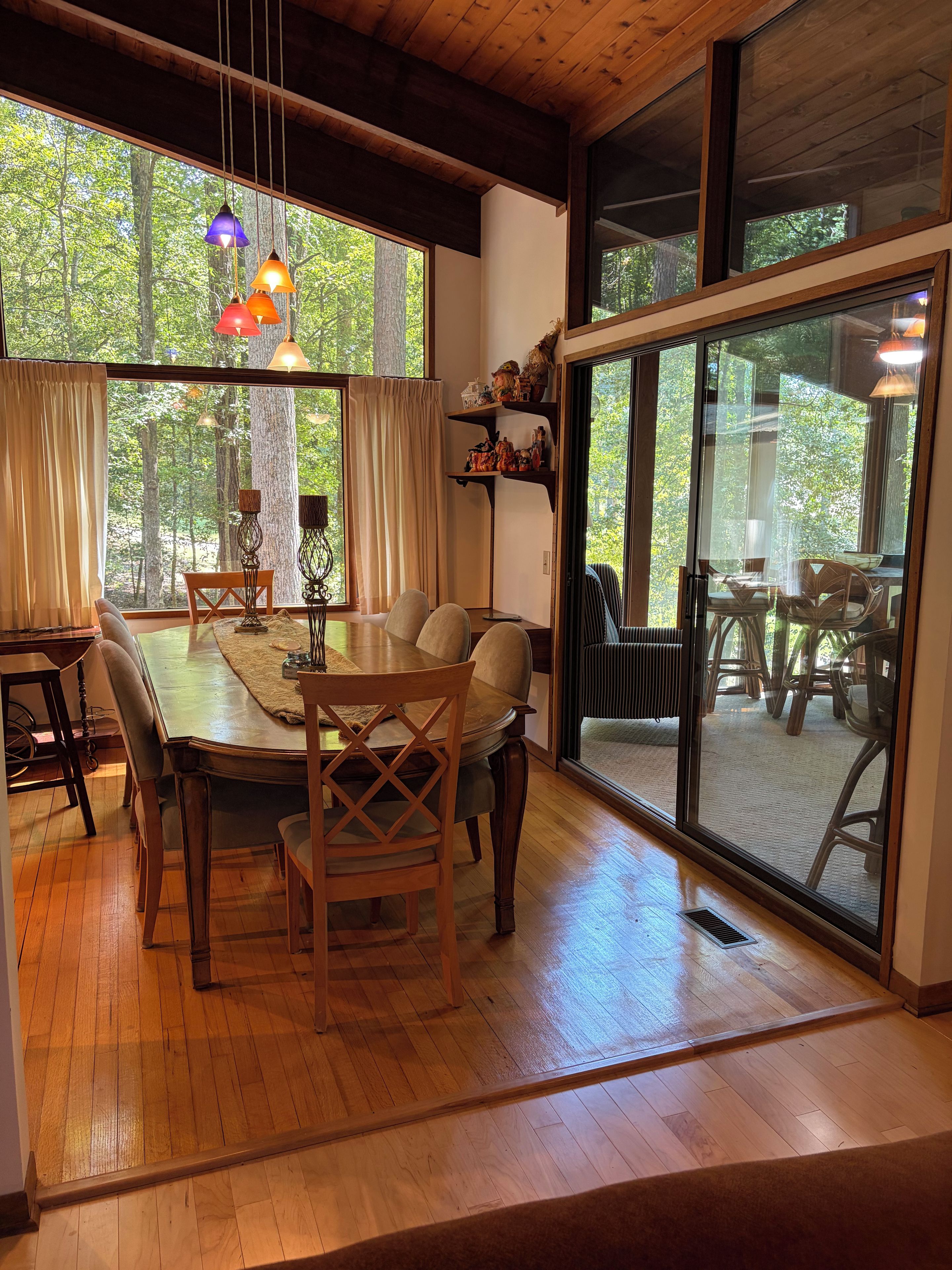 Un comedor con mesa de madera, sillas y vista a un bosque a través de amplios ventanales.