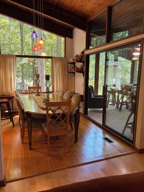 A dining area with a wooden table, chairs, and a view of a forest through large windows. - Private gorgeous retreat on the golf course in Carolina Trace (Sanford)