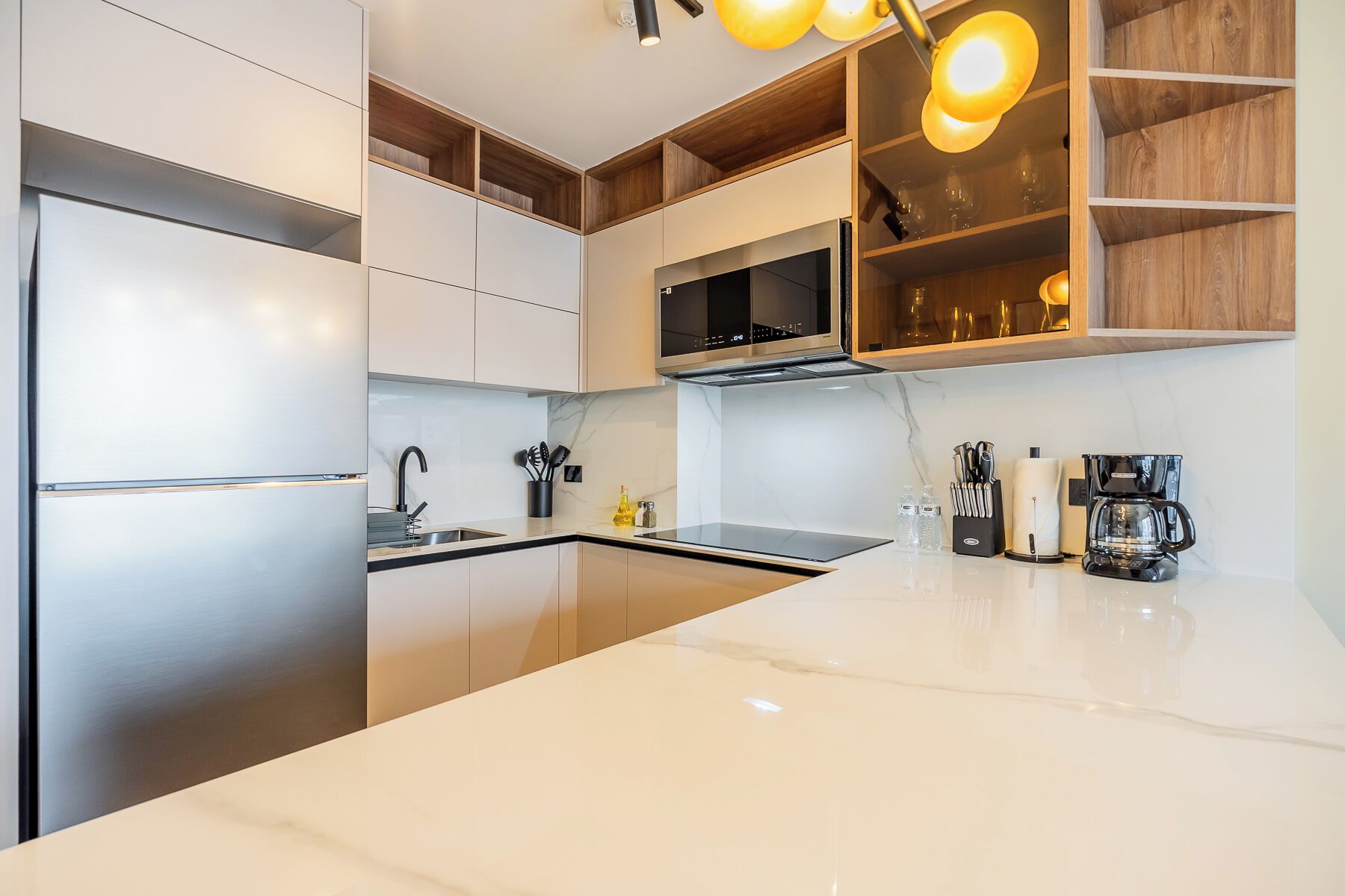 A modern kitchen with stainless steel appliances, a marble countertop, and wooden shelving.
