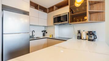 A modern kitchen with stainless steel appliances, a marble countertop, and wooden shelving.