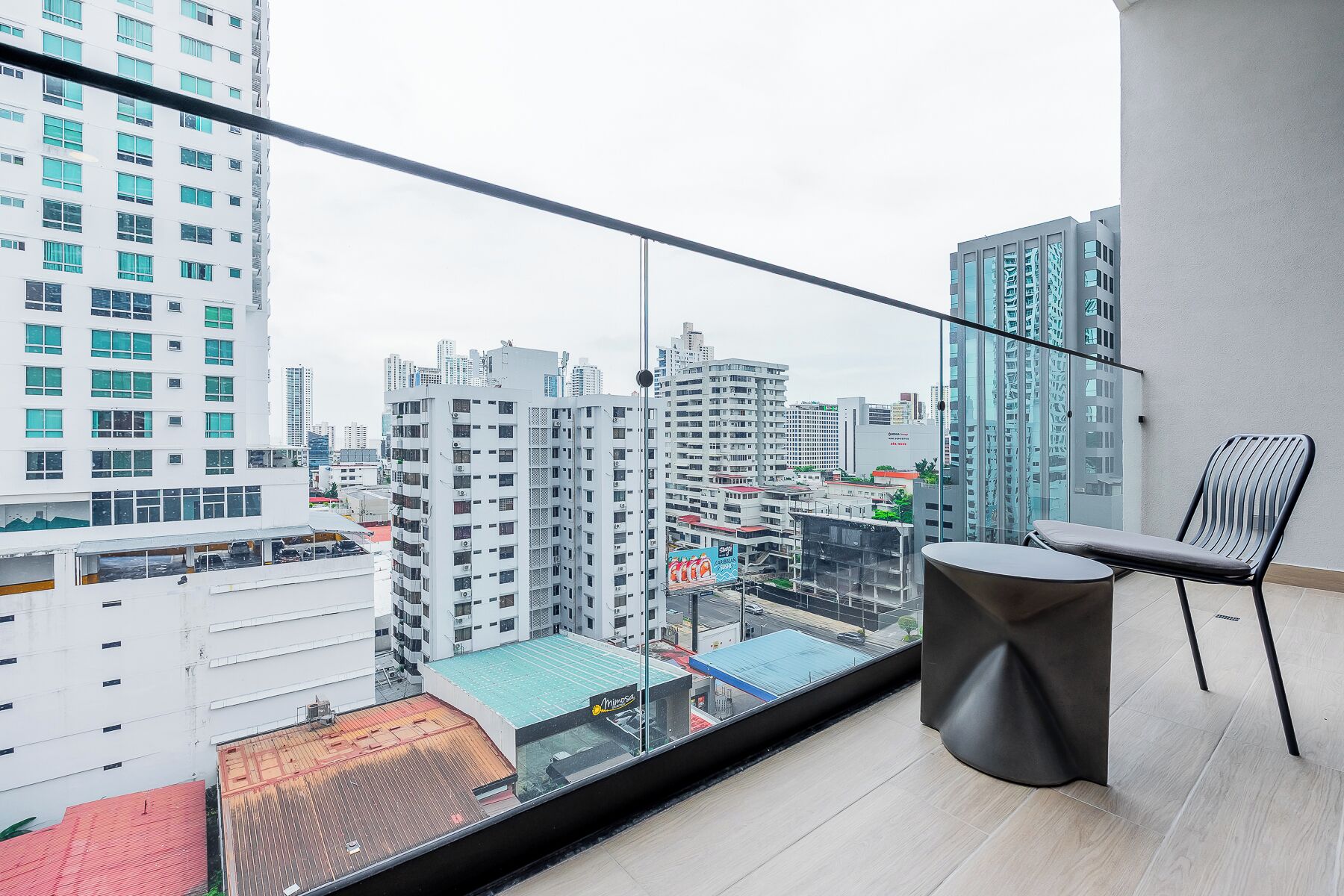 A balcony with a view of a cityscape, a round table, and a chair.