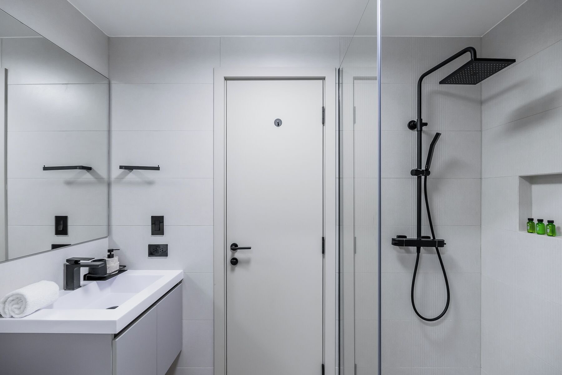 A modern bathroom with a glass shower enclosure, a white sink with a towel, and a door with a lock.