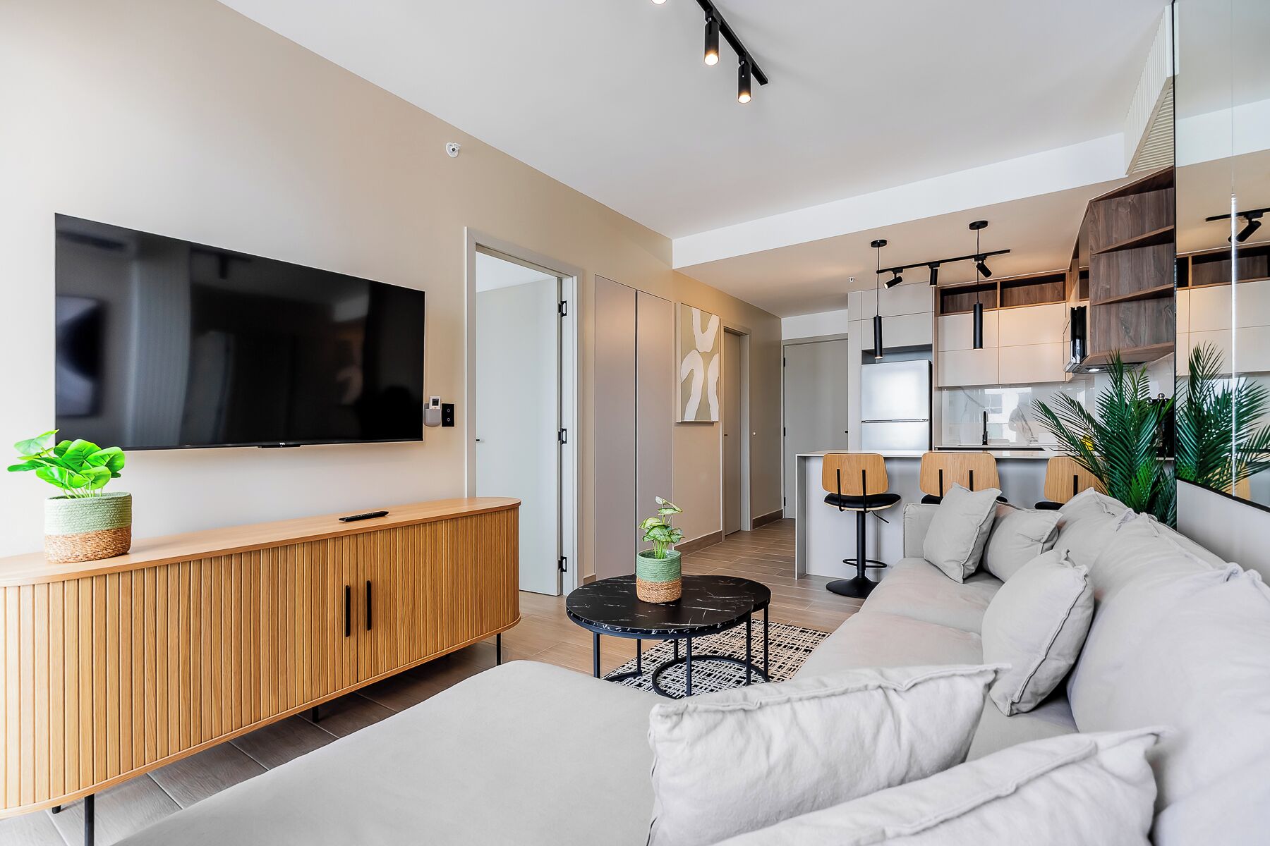 Una sala moderna con una televisión de pantalla plana, un mueble de madera, un sofá, una mesa de centro y una zona de comedor con sillas y una encimera de cocina.