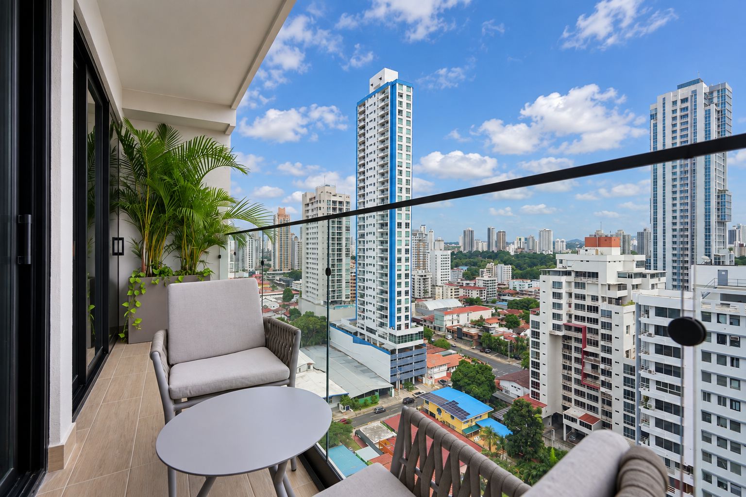Un balcón con sofá y mesa, con vistas a un paisaje urbano con edificios altos.