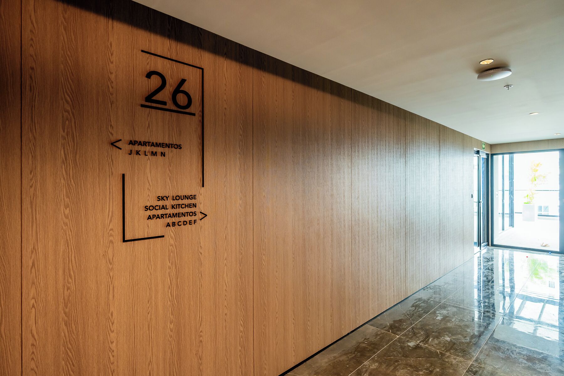 A hallway with a wooden wall, a number '26' sign, and directional arrows to amenities like 'Sky Lounge' and 'Social Kitchen'.