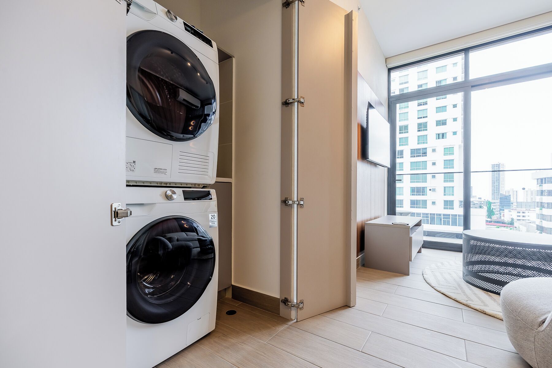 A modern apartment with a large window, a washing machine, and a small seating area.