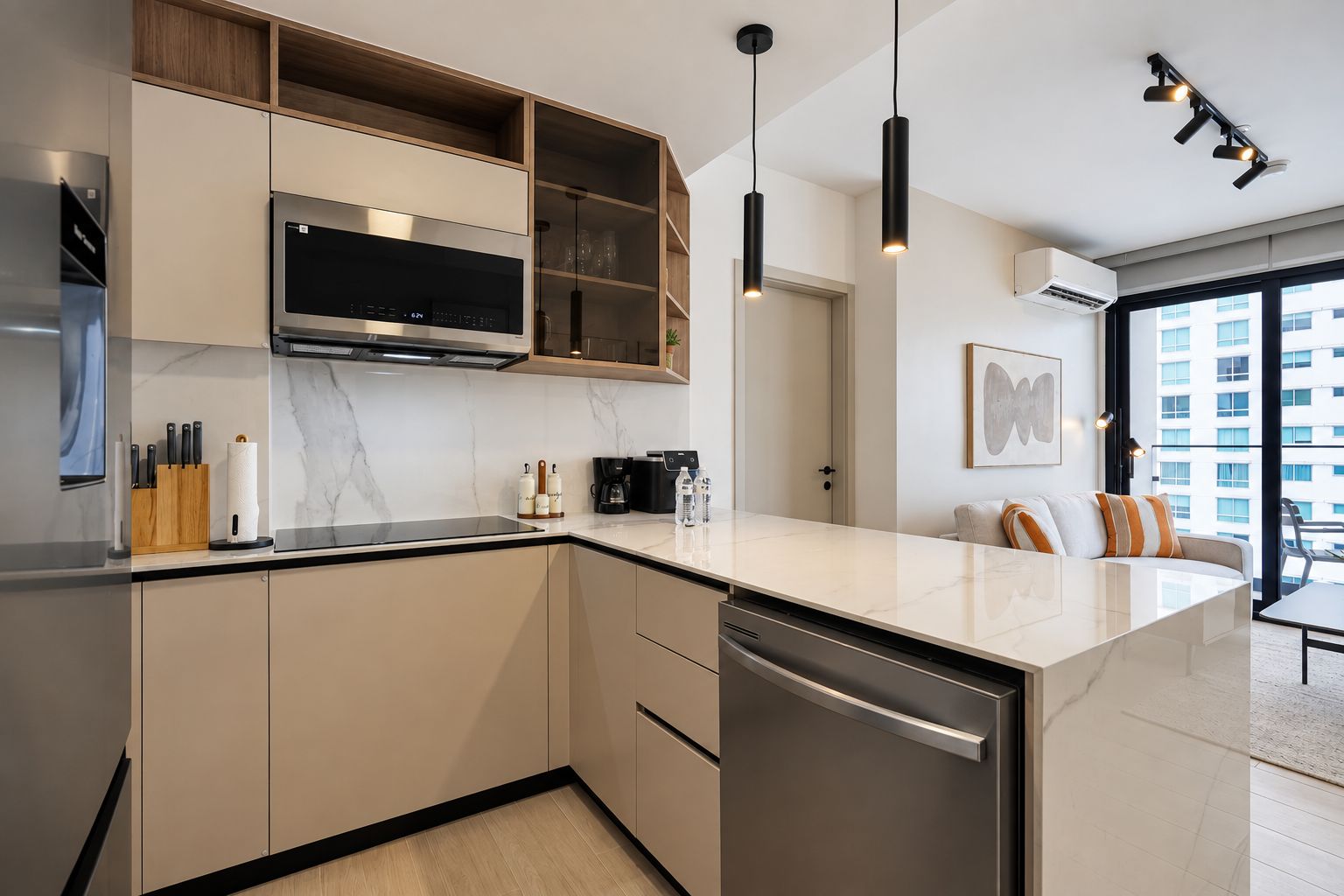 Una cocina moderna con horno empotrado, microondas y lavavajillas, armarios de madera e iluminación colgante.