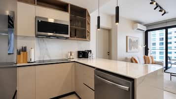 Une cuisine moderne dotée d’un four, d’un micro-ondes et d’un lave-vaisselle encastrés, de meubles en bois et de luminaires suspendus.