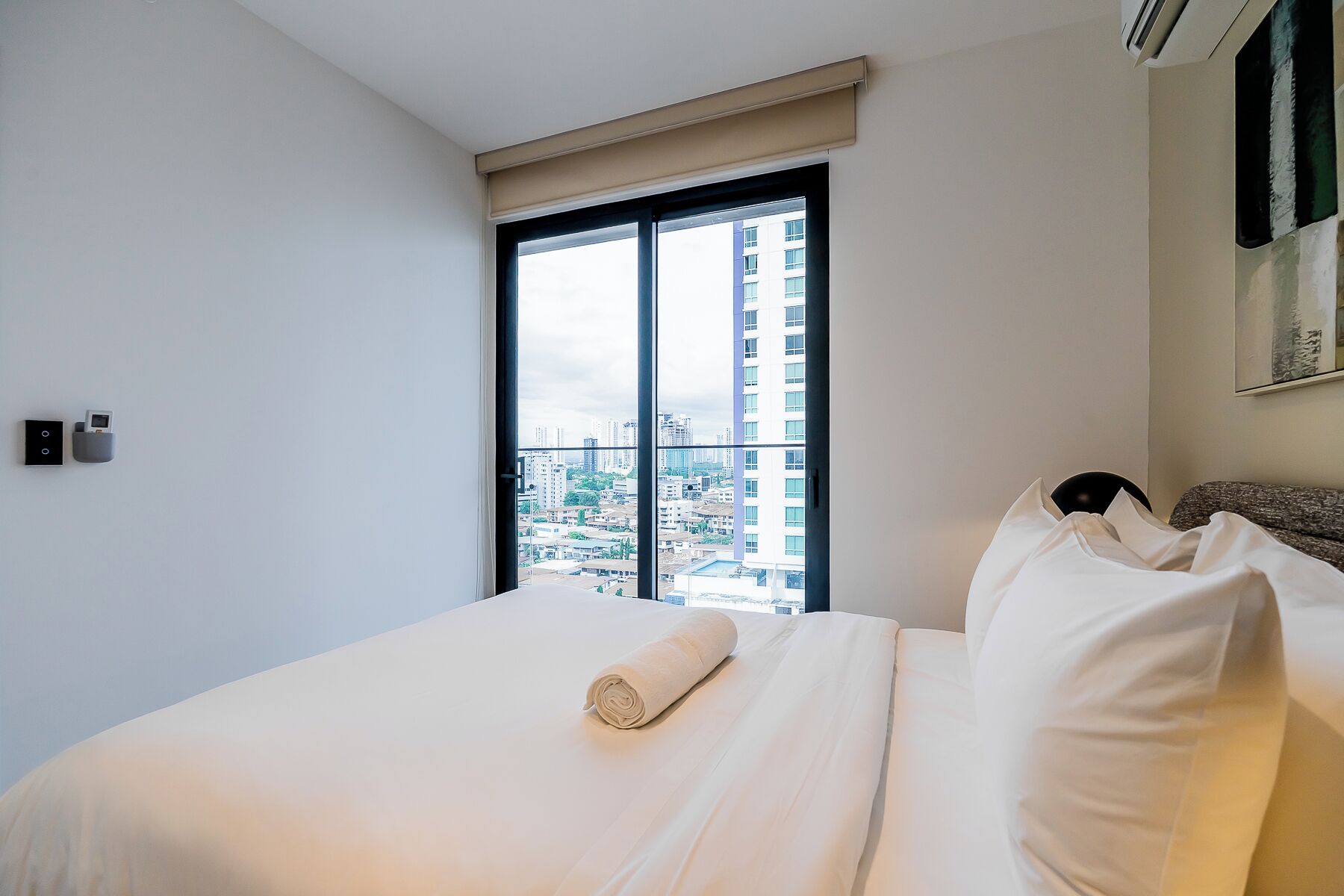 Habitación de hotel con una cama grande, una ventana con vista a la ciudad y un aire acondicionado instalado en la pared.