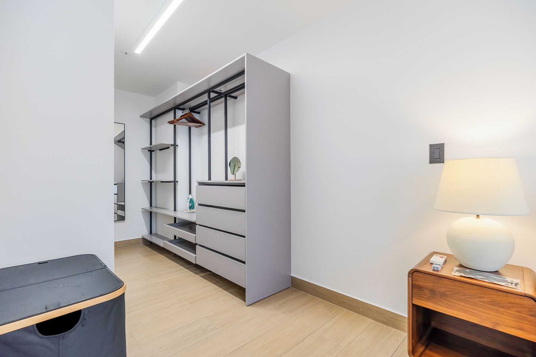Una habitación moderna con un armario, una mesita de noche con lámpara y un cesto de basura.