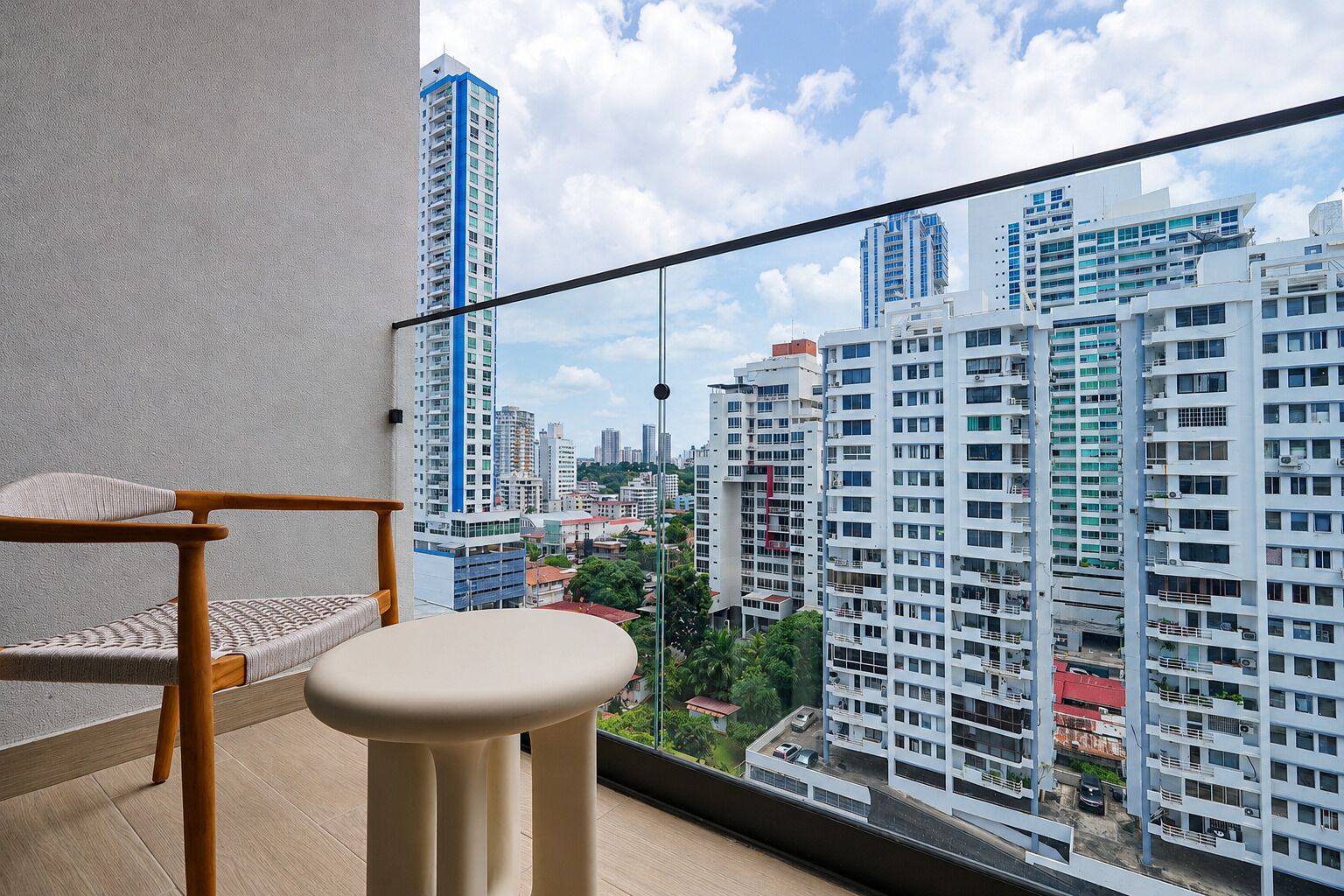 Un balcón con vistas a edificios altos, una silla de madera y un taburete.