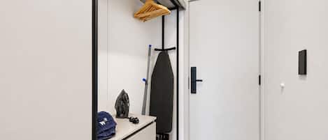 A modern closet with a hanging rack, an iron, and a blue towel on a shelf.