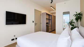 Ein modernes Hotelzimmer mit Bett, Wandfernseher, Kleiderschrank und Blick auf die Stadt durch ein Fenster.