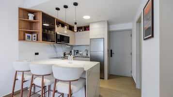 A modern kitchen with a marble countertop, stainless steel appliances, and wooden bar stools.