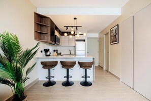 A modern kitchen with a central island, bar stools, and a potted plant. - The Hub Modern Apartments by Wynwood (Panamá)