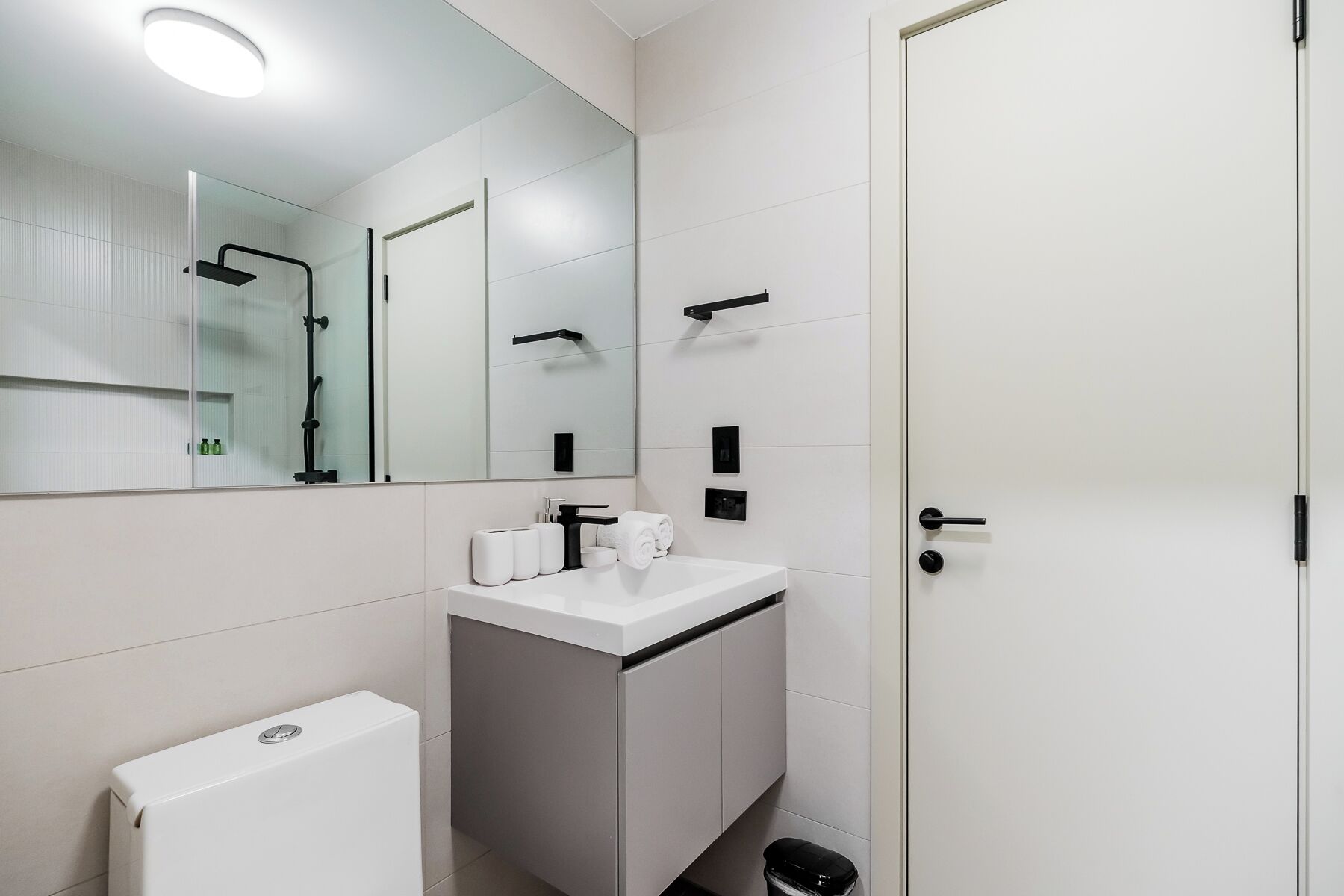 Un baño moderno con lavamanos, espejo y retrete blancos.