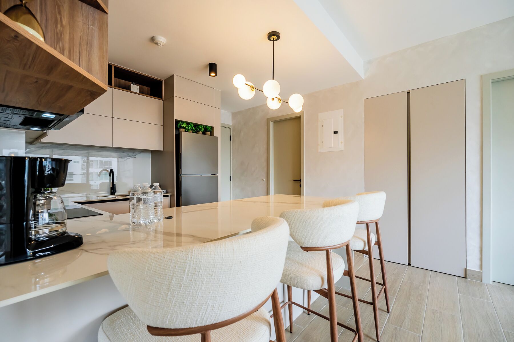 A modern kitchen with a central island, bar stools, and a coffee machine.