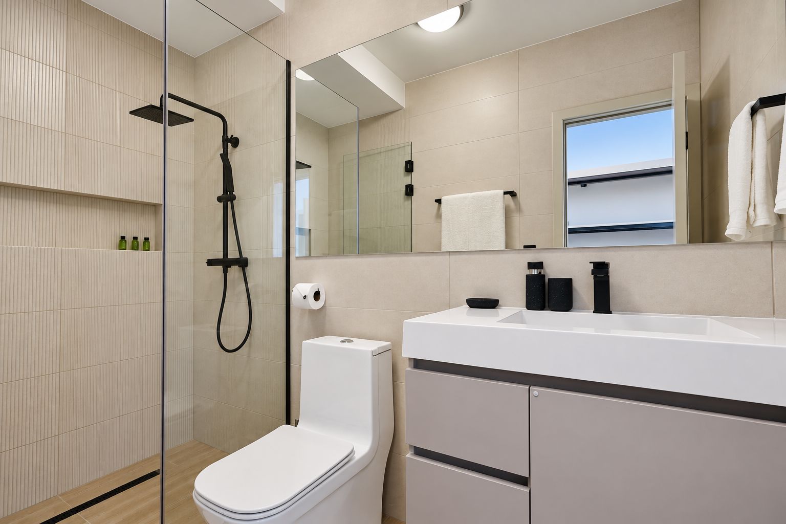 A modern bathroom with a glass-enclosed shower, a white toilet, and a large mirror above the sink.